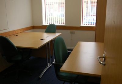 Small three-person office with light wood desks and green chairs.