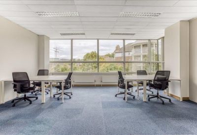 Bright open-plan office space with two white desks and black ergonomic chairs by a large window.