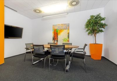 Modern meeting room with a wooden table, vibrant orange feature wall, and a large plant.