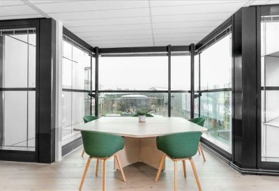 Bright breakout space with a hexagonal table and green chairs surrounded by glass partitions.