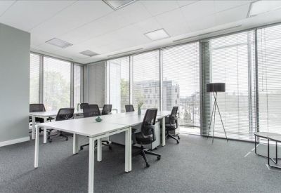 Bright open-plan office space with white desks, ergonomic chairs, and large floor-to-ceiling windows.