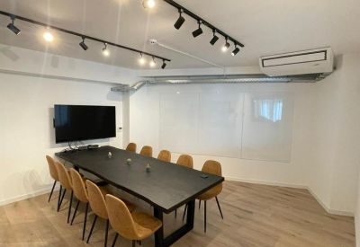 Bright conference room with a long black table, tan chairs, and a flat-screen TV.