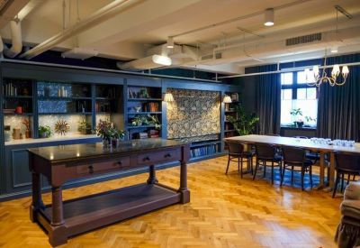 Communal break area featuring a dark wooden island and a long dining table under high ceilings.