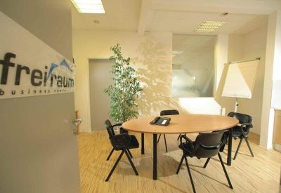 Modern office reception area with a wooden table, green plant, and branded signage.