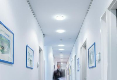 Bright, white corridor featuring framed artwork and a person walking in the distance.