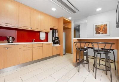 Office kitchen and break area with wooden cabinetry, red backsplash, and breakfast bar seating.