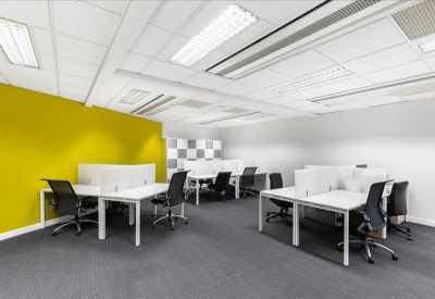 Bright open-plan coworking space with a vibrant yellow feature wall and white desks.