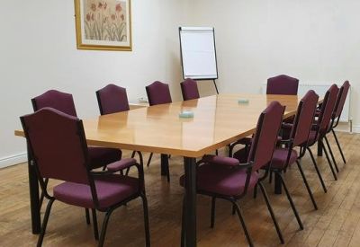 Functional meeting room with a large wooden table, purple chairs, and a whiteboard.