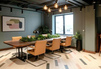 Long wooden meeting table with tan leather chairs and a green plant centerpiece.