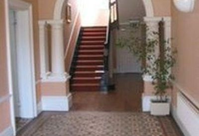 Grand hallway featuring decorative floor tiles, white pillars, and a central staircase.