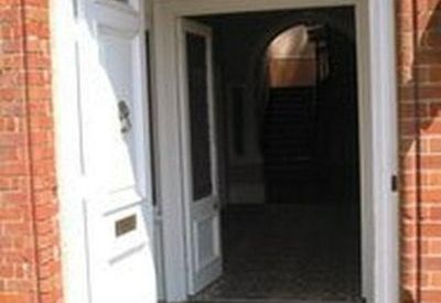 Arched brick entrance with a large white front door and view into the lobby.
