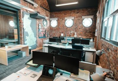 Coworking space with exposed brick walls, circular windows, and multiple monitor setups.