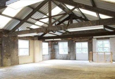 Spacious open-plan office shell with industrial timber roof trusses and large windows.