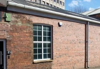 Side view of a red brick industrial building with large multi-pane windows.