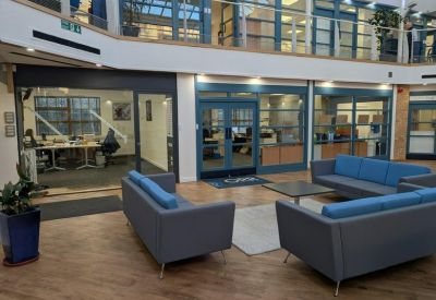 Lounge area with modern blue sofas and glass-fronted office suites in the background.