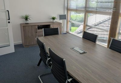 Professional meeting room with a wooden table, ergonomic black chairs, and large windows with blinds.