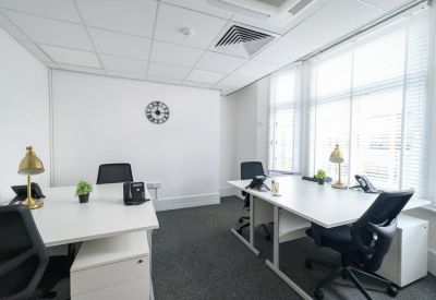 Bright, white office space featuring several workstations with gold desk lamps and ergonomic chairs.