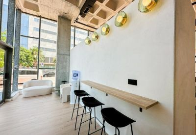 Modern break area with high black stools and a wooden bar counter against a white wall.
