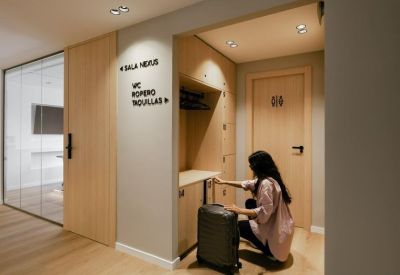 Signage and storage lockers in a bright hallway with a person and their luggage.