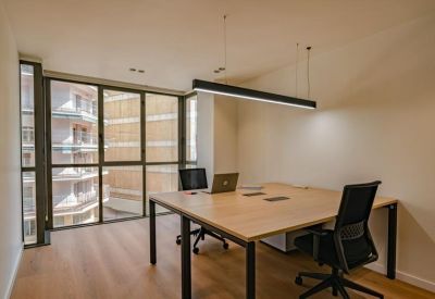 Modern office with a wooden shared desk and large windows overlooking city buildings.