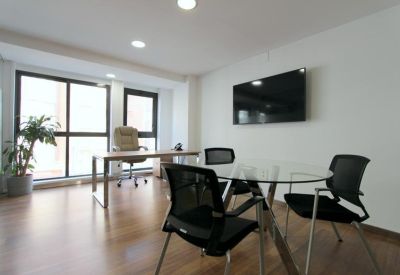 Professional meeting space with a glass table, black chairs, and wall-mounted screen.