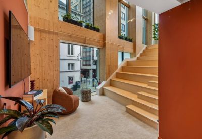 Modern wooden staircase area with a cozy brown armchair and views of the city through large windows.