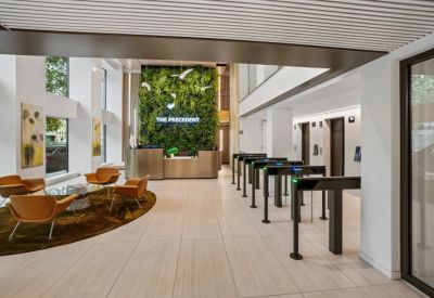 Modern lobby with a green plant wall, sleek reception desk, and orange lounge seating near security gates.