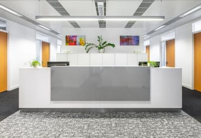 Sleek minimalist reception desk with green plants and bright overhead lighting.