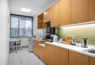 Modern office kitchen with light wood cabinetry and various coffee appliances.
