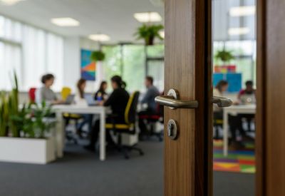 View through a wooden doorway into an open-plan office with people at desks.