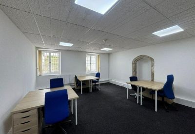 Bright private office suite with three wooden desks and blue chairs under modular lighting.