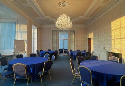 Grand meeting room with blue-clothed circular tables, ornate ceiling, and a large crystal chandelier.