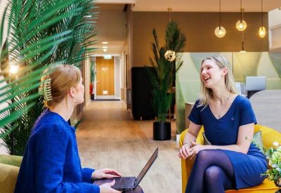 Two women talking on colorful armchairs in a vibrant coworking area.