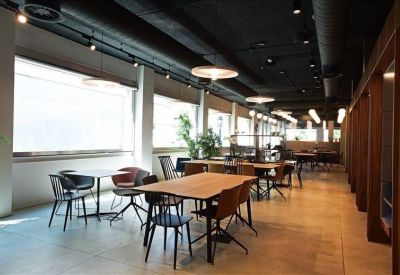 Long communal dining or coworking area with wooden tables and industrial ceiling.