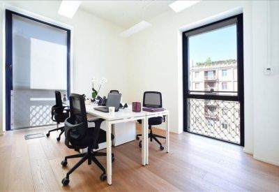 Bright shared office space with white desks and black mesh chairs.
