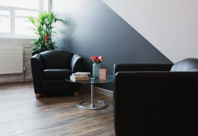 Bright breakout area with leather armchairs and a glass coffee table near a window.