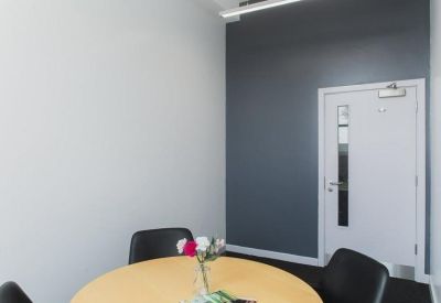 Private meeting room with a round table, black chairs, and a grey accent wall.