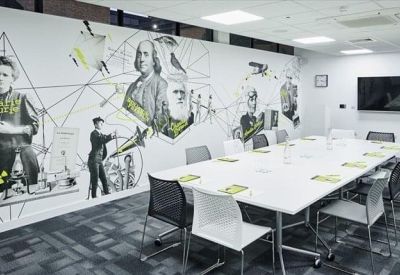 Modern meeting room featuring a wall mural of historical figures and a white conference table.
