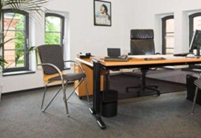 Bright private office suite with a large wooden desk, ergonomic chairs, and potted palm plant.