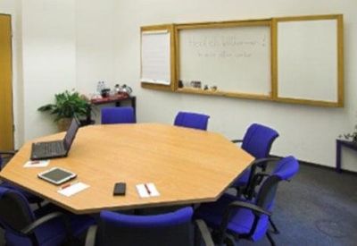 Octagonal wooden meeting table surrounded by blue chairs with a whiteboard and laptop.