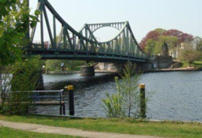Scenic view of a blue steel suspension bridge over a river surrounded by lush green trees.