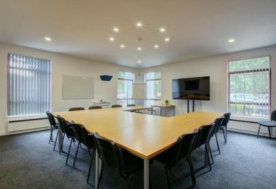 Meeting room with a large light-wood table arranged in a U-shape and a wall-mounted TV.