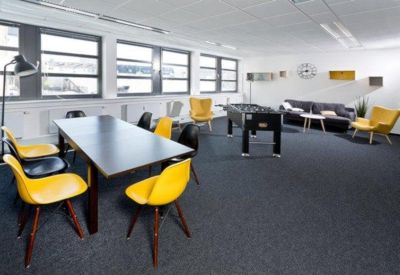 Bright communal lounge featuring yellow chairs, a foosball table, and a grey sofa area.