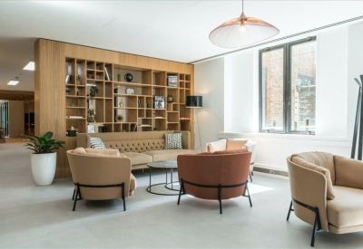 Stylish lounge with tan armchairs and a large wooden bookshelf partition.