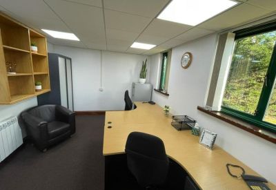 Private office suite with an L-shaped desk, black armchair, and wooden shelving unit.