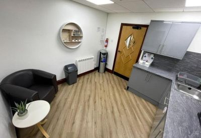 Communal break area with a black armchair, circular shelf, and kitchenette cabinets.