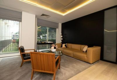 Modern lounge with a tan leather sofa, wooden armchairs, and a black feature wall.