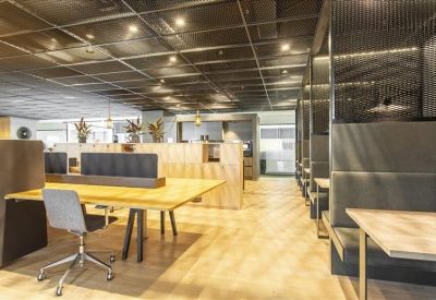 Spacious coworking lounge with wooden flooring and industrial-style mesh ceiling.