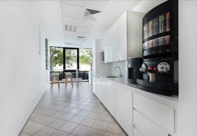 Sleek white office kitchen area with coffee machine and breakfast bar seating.
