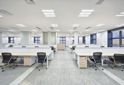 Spacious open-plan workspace with rows of modern white desks and black mesh ergonomic chairs.